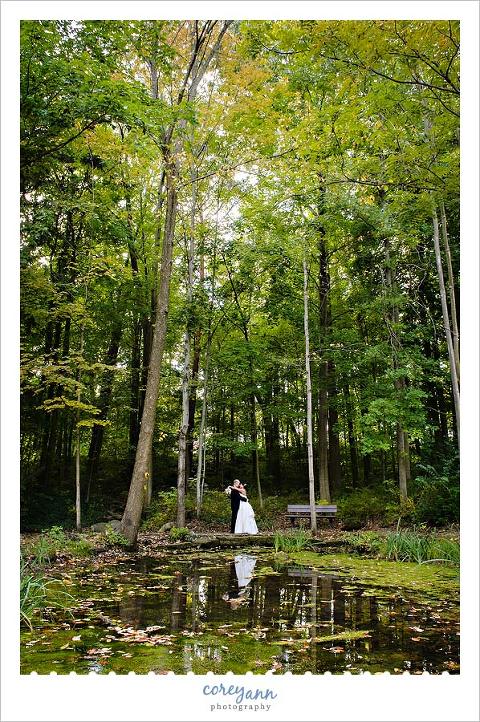 bride and groom in forest with reflection on pond during the fall