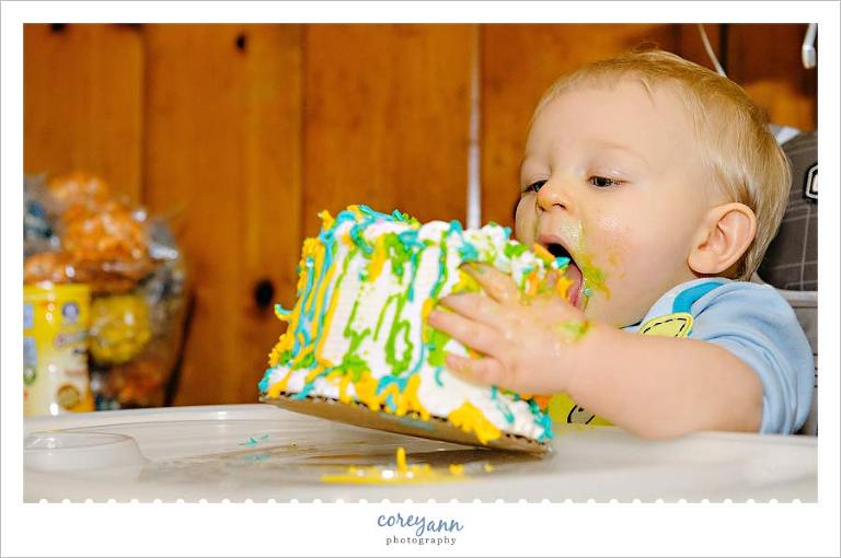 one year old picking up his cake to eat it at his party
