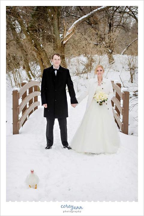 bride and groom posing outside with a duck