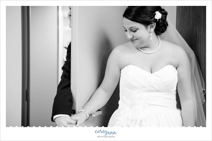Nancy Bride Talk bride and groom holding hands on either side of the door as a first look before wedding