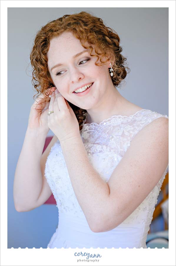 bride putting earrings in while getting ready for wedding