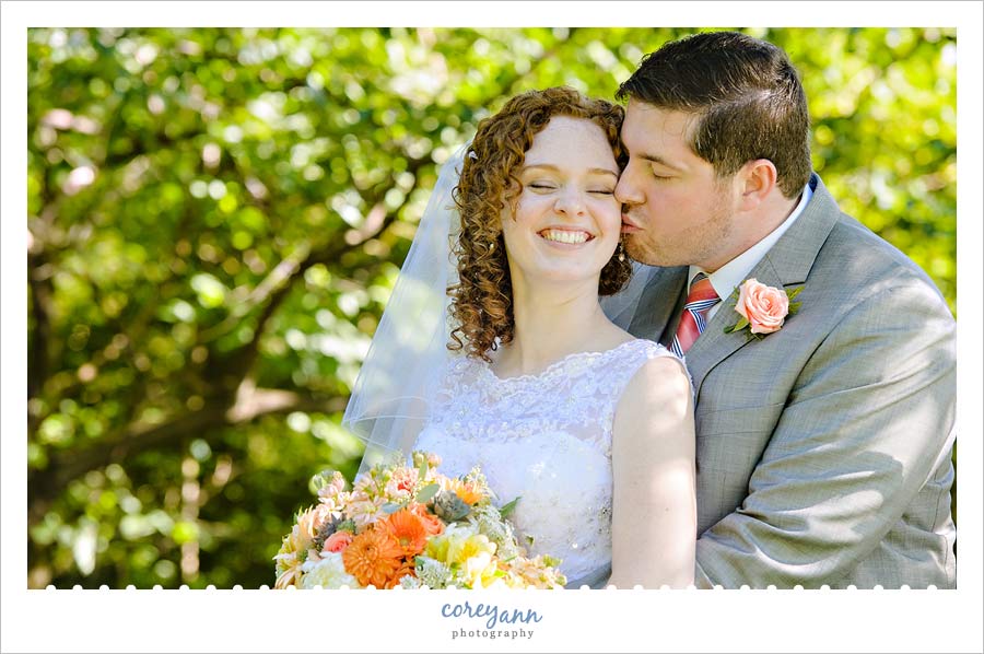 groom kissing bride on the cheek outside