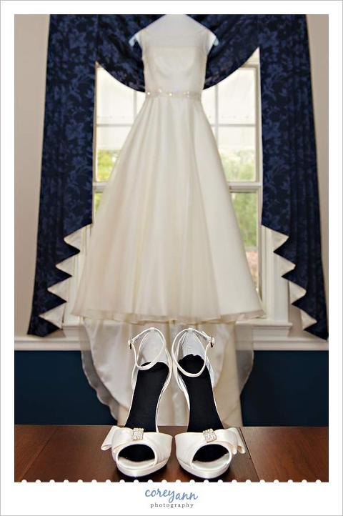 white wedding dress on hanger with shoes in front of it