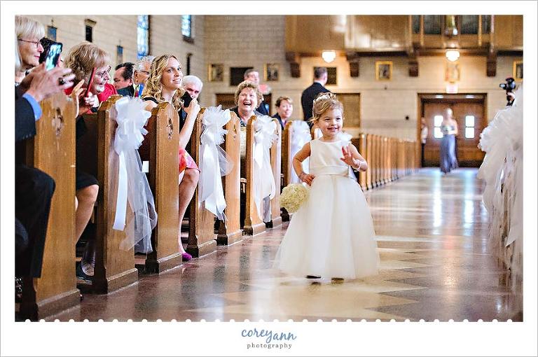 flower girl waving as she walks up the aisle at wedding ceremony
