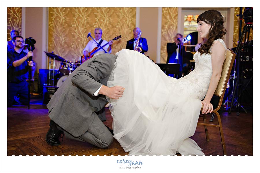 groom taking garter off with his teeth at wedding reception
