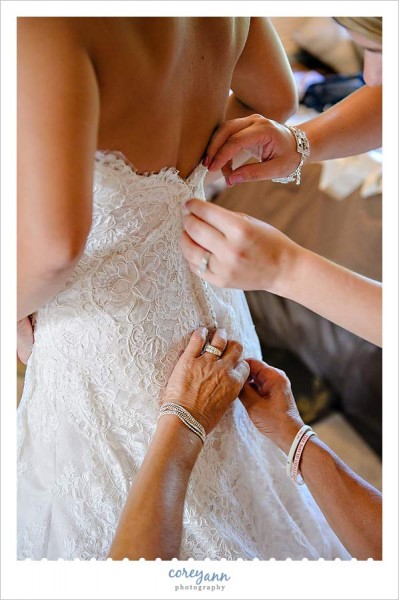 bridesmaids and mother doing buttons on bride's dress
