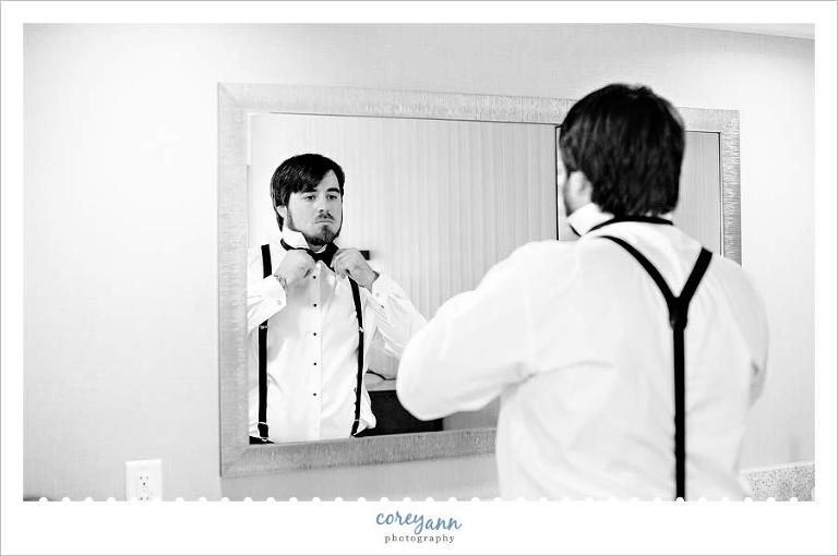 groom tying bow tie in mirror before wedding