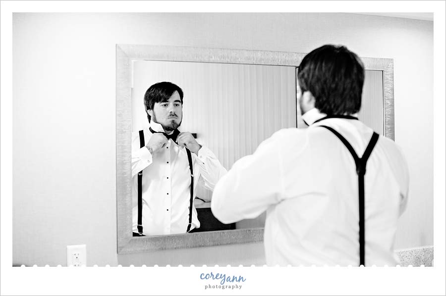 groom tying bow tie in mirror before wedding