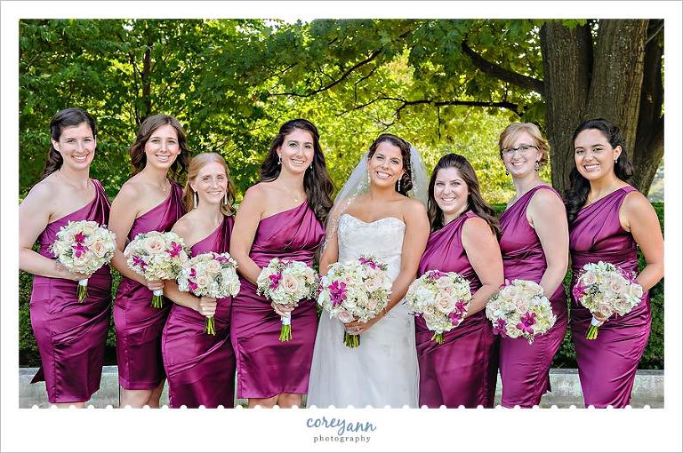 bride and bridesmaids in short satin purple one shoulder bridesmaid dresses with orchid bouquets
