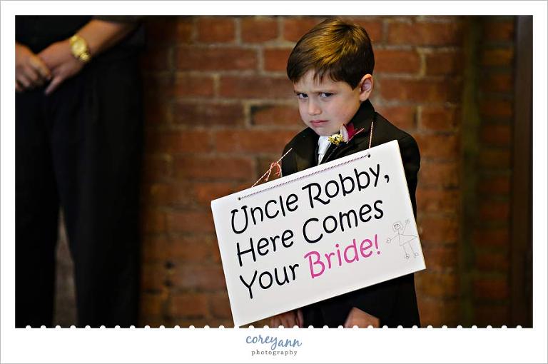 unhappy ring bearer with here comes your bride sign