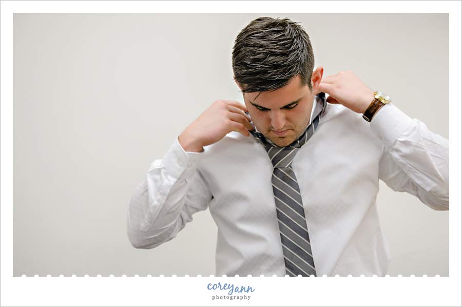 Groom adjusting his necktie before wedding at walsh university in Ohio