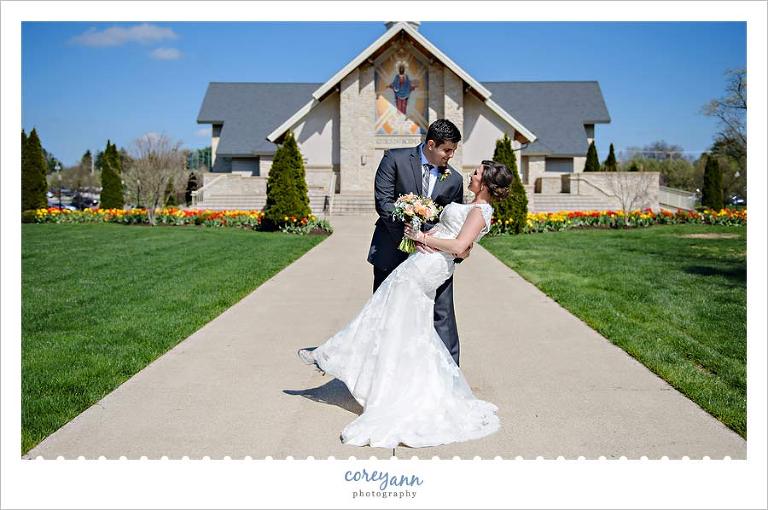 Groom dips bride in front of chapel with tulips and blue skies