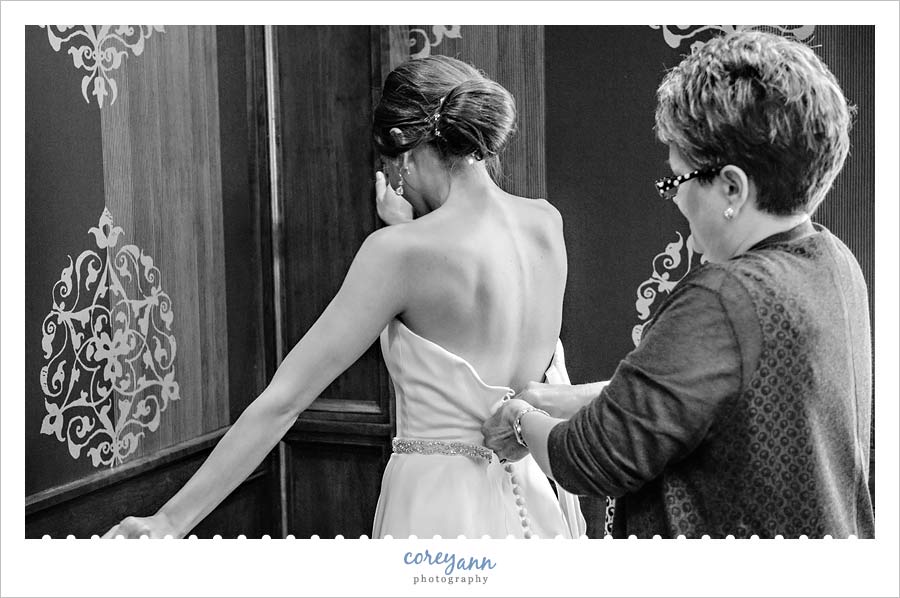 bride's mother doing up buttons on back of wedding dress