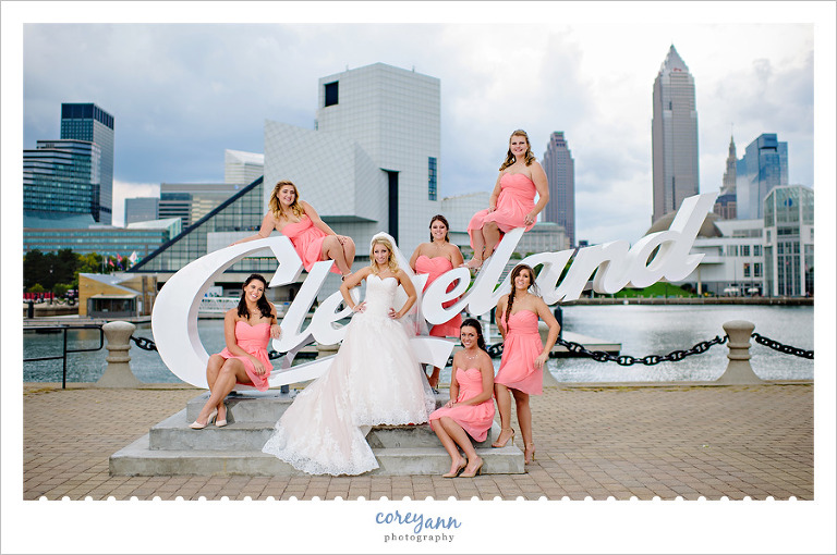 bridesmaids in short coral dresses posing with bride on cleveland script sign