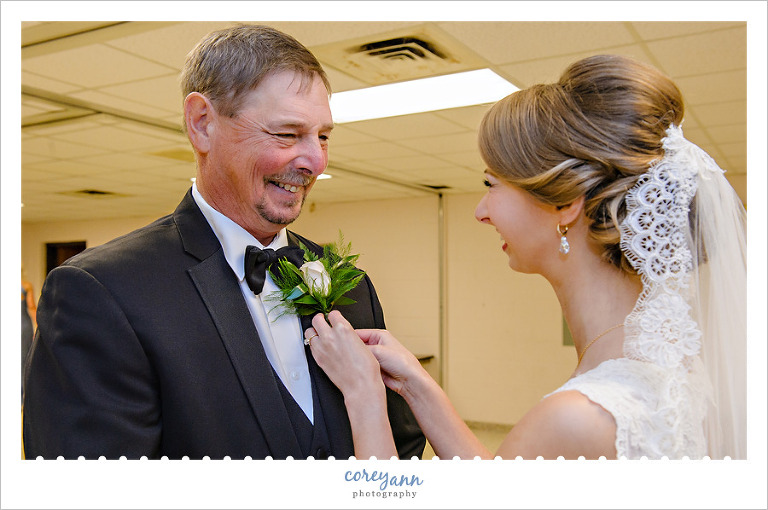 Bride pinning boutonniere on father before wedding