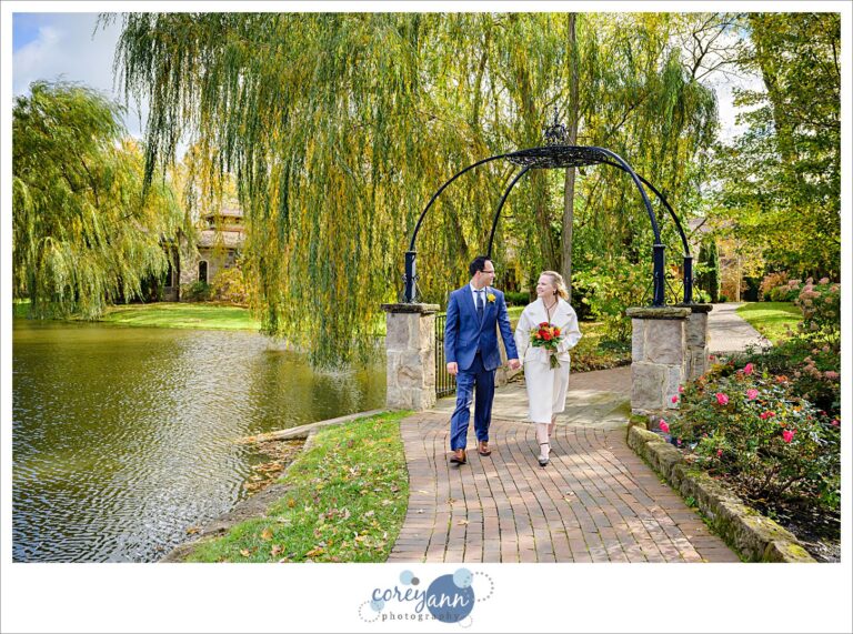 A bride and groom walking along a path near a pond at Gervasi Vineyard in Ohio on their wedding day.