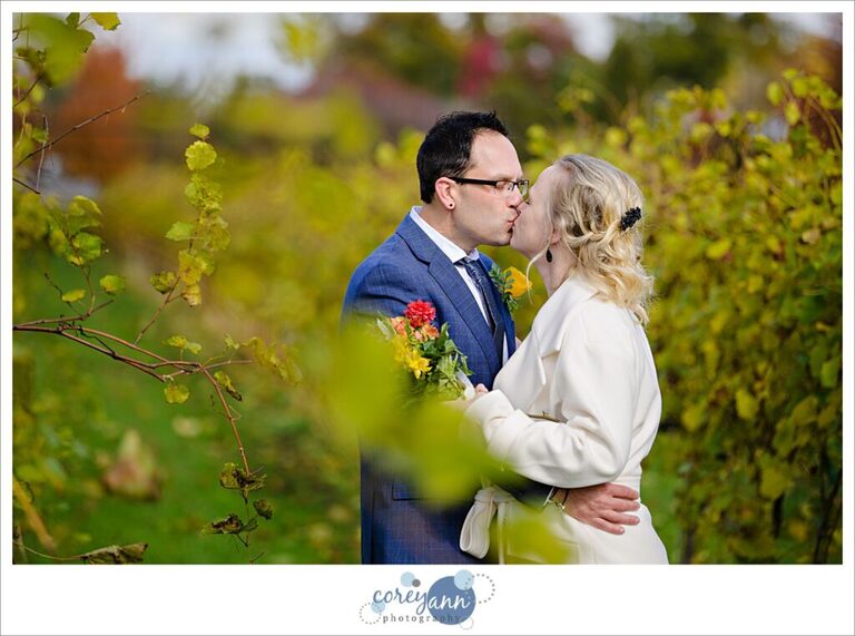 A bride and groom kissing after their wedding with foliage around the turning colors at Gervasi Vineyard on their wedding day.