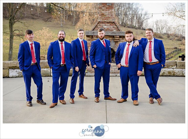 Groomsman posing casually wearing red ties with blue suits and cowboy boots