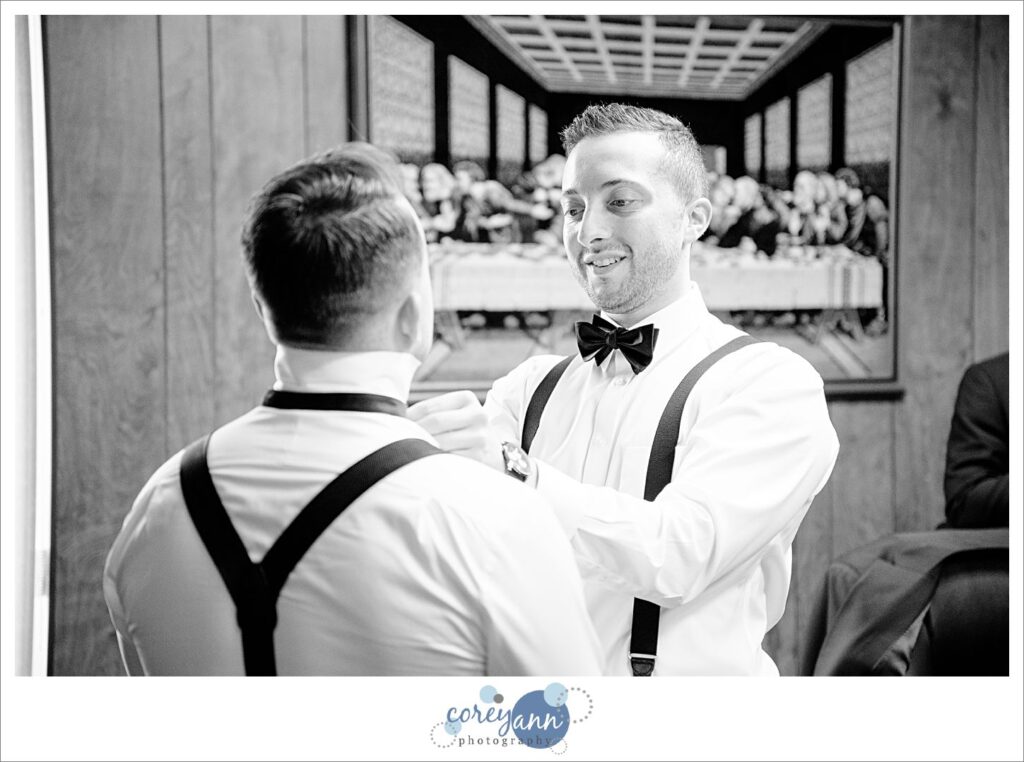 Groomsman helping groom with bow tie before wedding in Canton Ohio