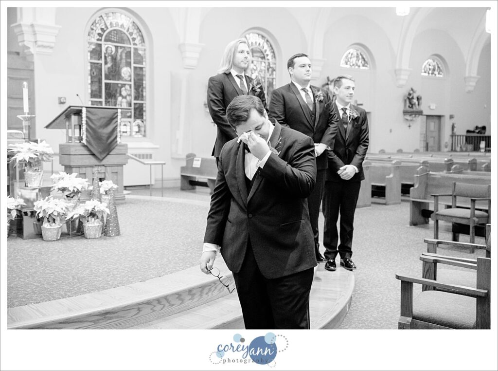 Groom wiping tear from his eye when watching bride walk down aisle at wedding ceremony