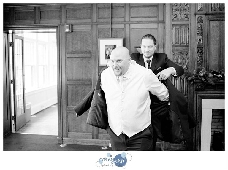 Groomsman helping groom get into coat at Henn Mansion on a wedding day
