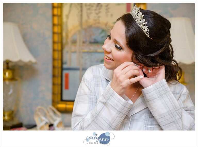 Bride wearing a tiara in wedding pajamas putting earrings in