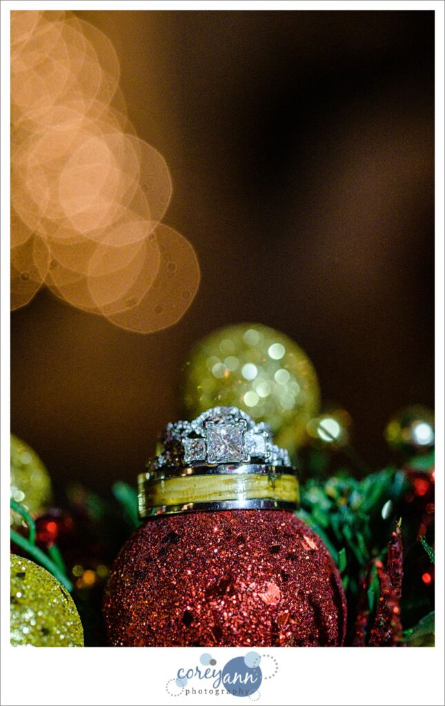 Wedding rings balanced on christmas ornaments with twinkle lights in the background