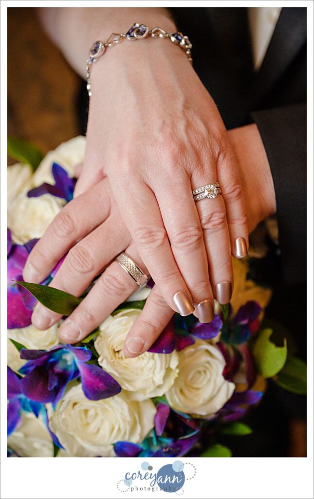 Hands with wedding rings posed on top of wedding bouquet 