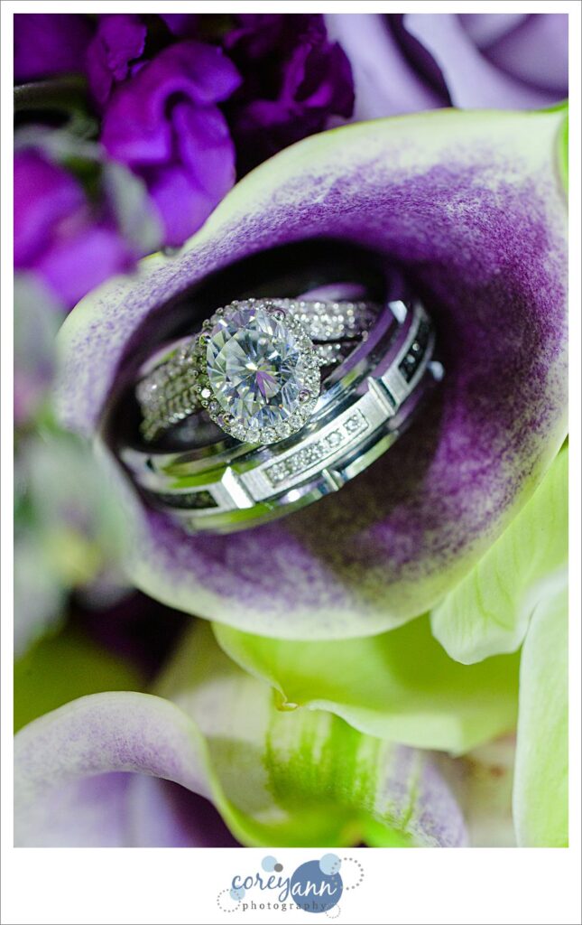 Oval engagement ring and wedding bands on purple lilly in wedding bouquet