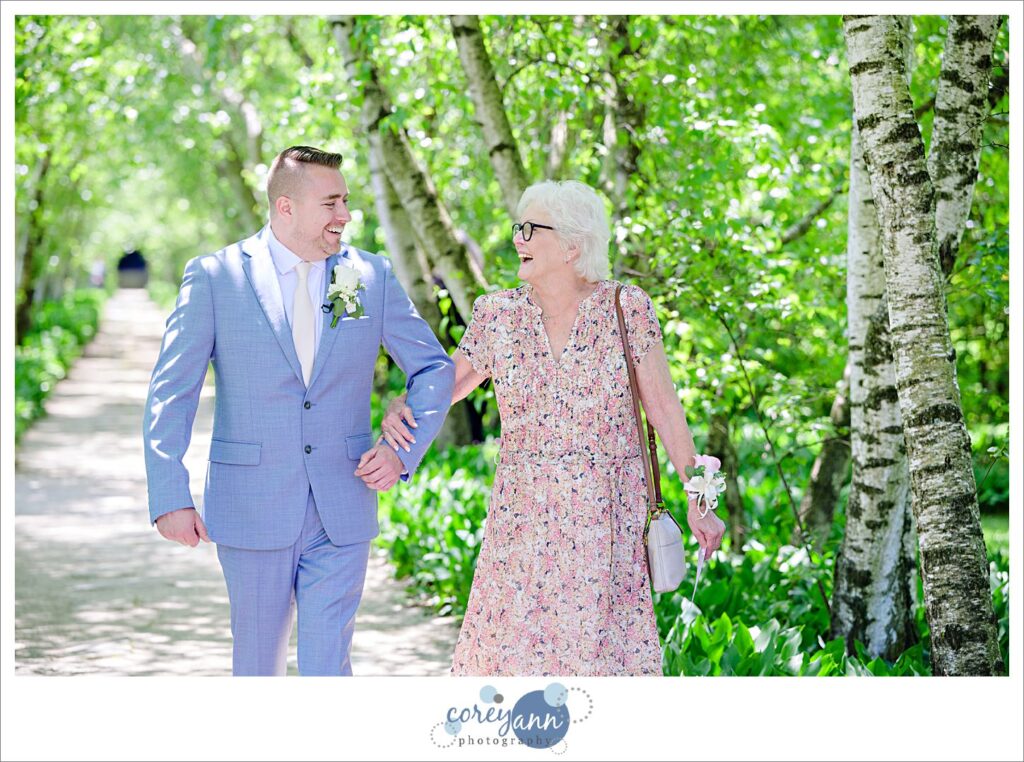 Groom walking his mother down the birch tree allee aisle to wedding ceremony at Stan Hywet