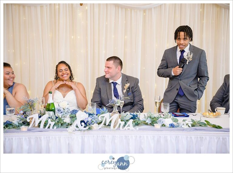 A bride and groom sitting while one of their bridal party gives a toast during the wedding reception in Akron Ohio
