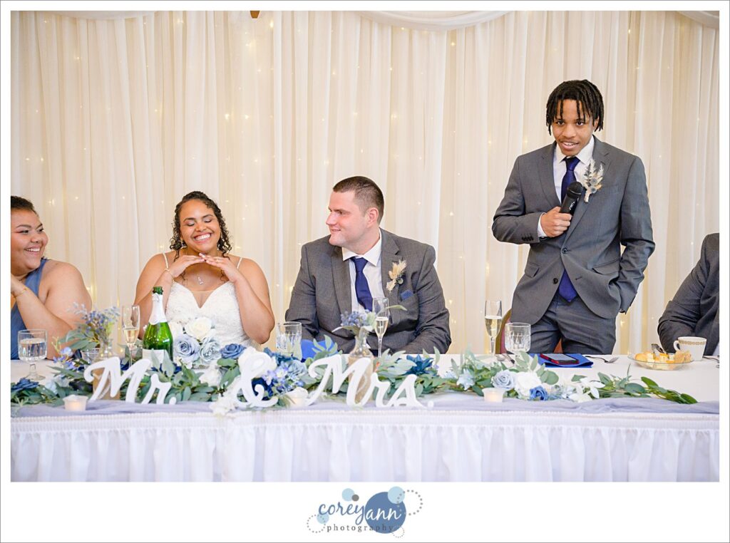 A bride and groom sitting while one of their bridal party gives a toast during the wedding reception in Akron Ohio
