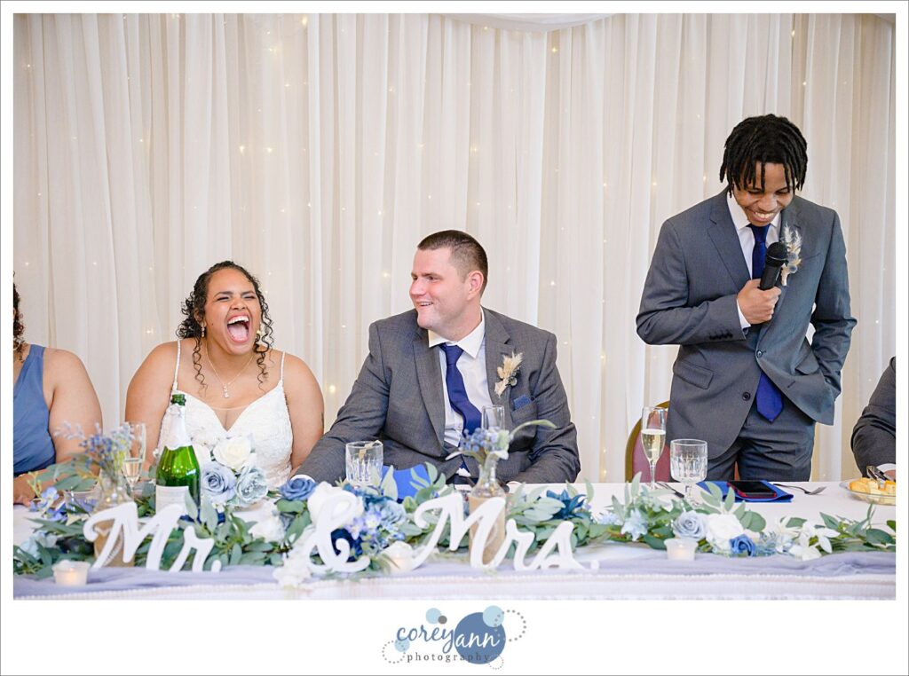 A bride and groom sitting while one of their bridal party gives a toast during the wedding reception in Akron Ohio