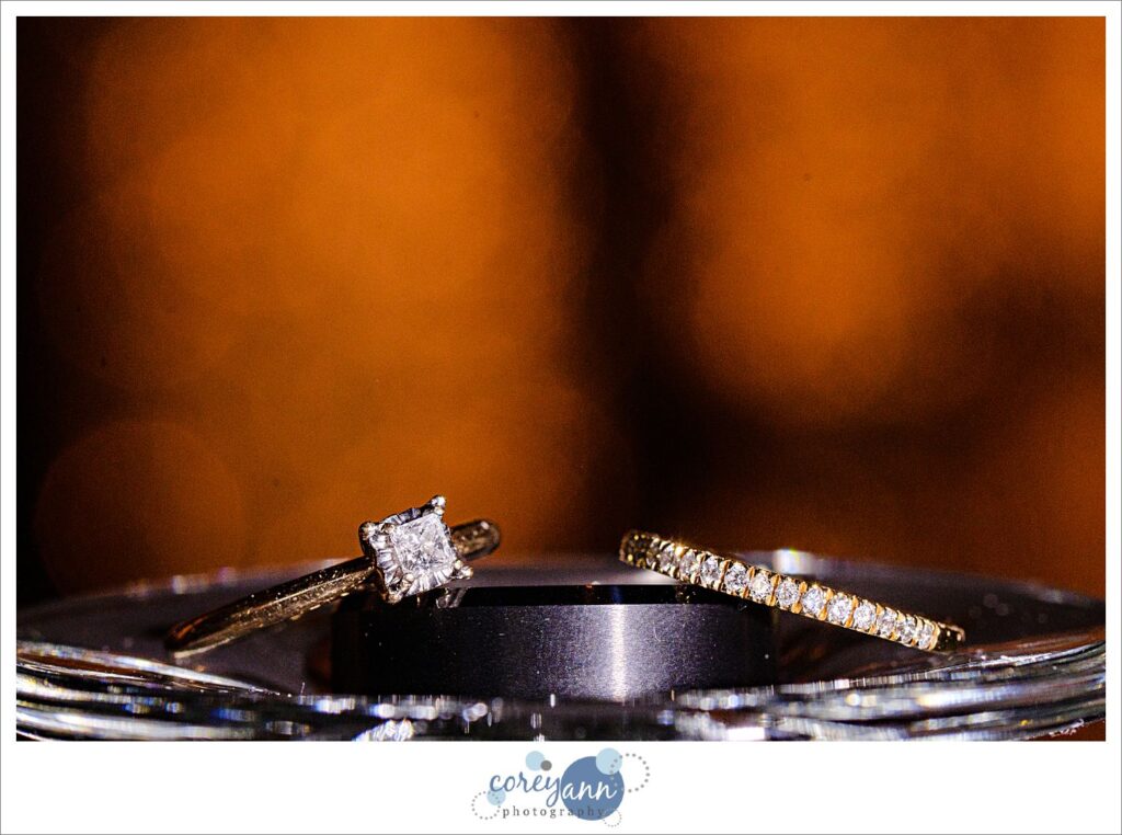 Engagement ring and two wedding bands placed in a stack with blurry lights in the background