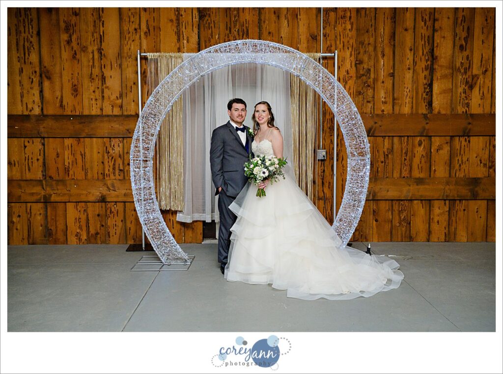 Bride and groom posing beneath a ceremony arch inside Amy's Rustic Event Center before their wedding in Valley City, Ohio