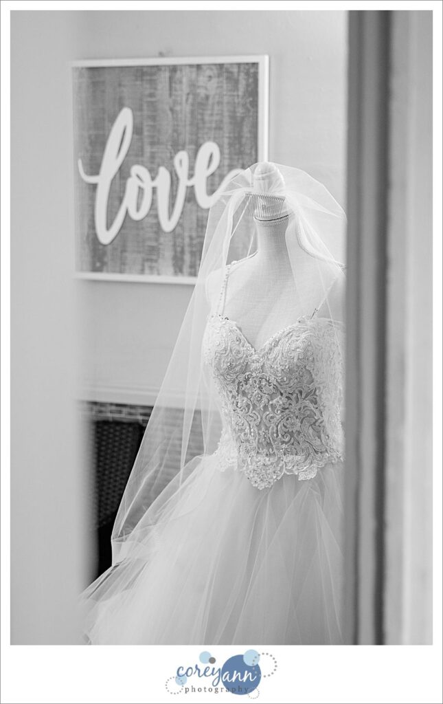 black and white photo of a wedding dress on a dress form in front of a "love" sign before a wedding