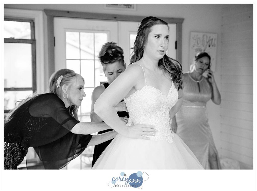 Black and white photo of a bride being buttoned into her wedding dress that is form fitted with spaghetti straps before her wedding in Valley City Ohio