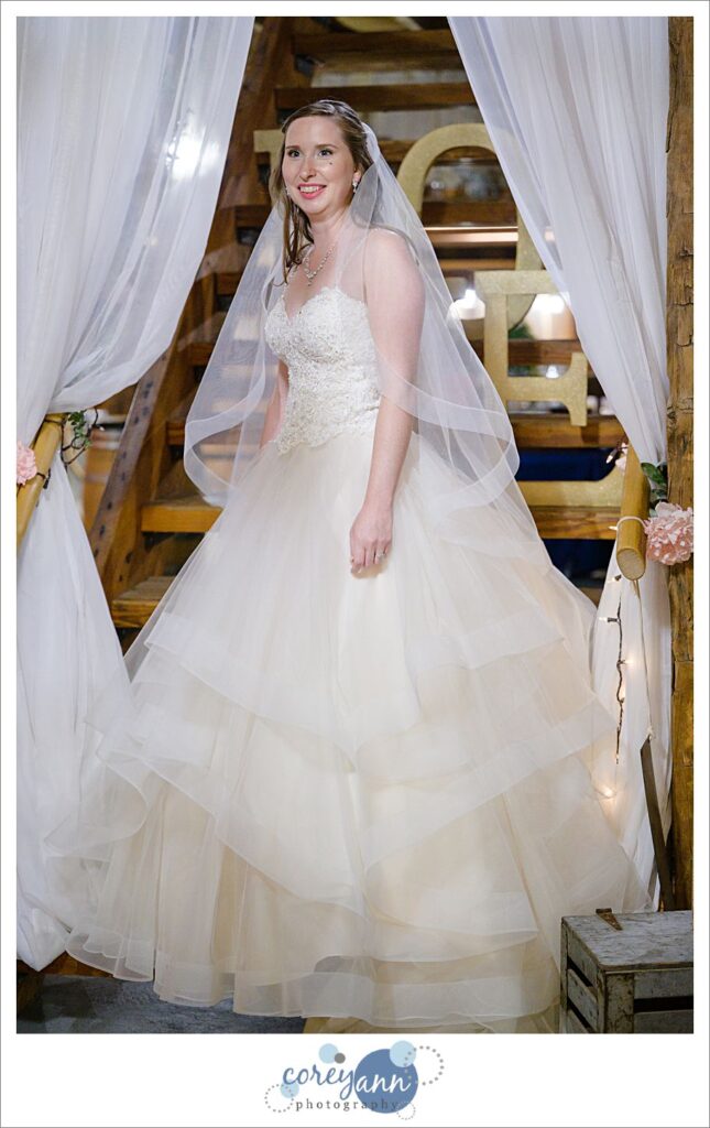 A bride in a white wedding dress with a full skirt with layers wearing a veil standing on stairs at Amy's Rustic Event Center in Valley City, Ohio