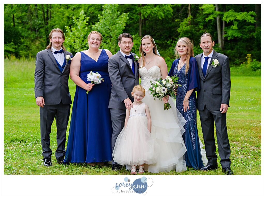 A family portrait before a wedding at Amy's Rustic Event Center in Valley City Ohio taken outside in the grass with the bride and groom, her parents, their daughter, her brother and his wife. All are smiling and wearing formal clothing. 