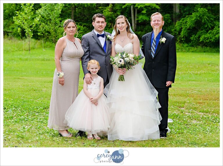 A family portrait before a wedding at Amy's Rustic Event Center in Valley City Ohio taken outside in the grass on a sunny June day with the bride and groom, his parents, and their daughter. All are smiling and wearing formal clothing. 