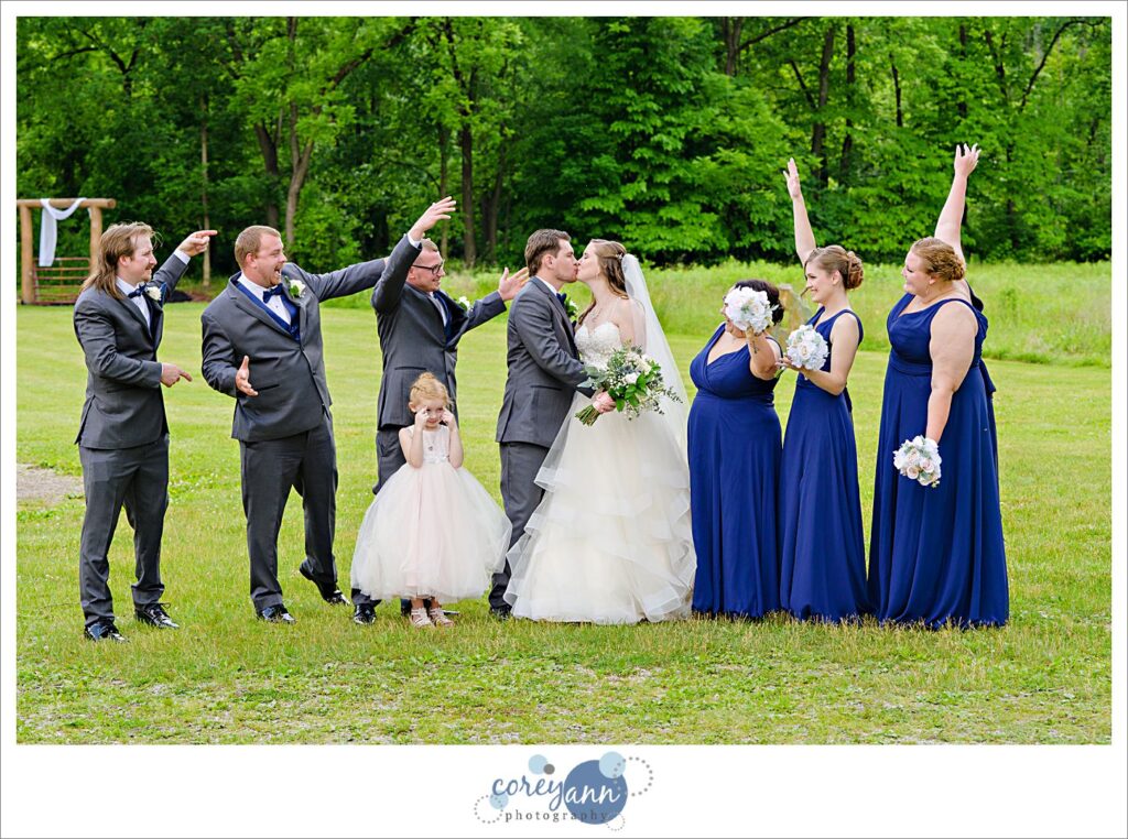 Bride and groom kissing while their bridal party cheer wedding at Amy's Rustic Event Center in Valley City Ohio taken outside in the grass on a sunny June day.
