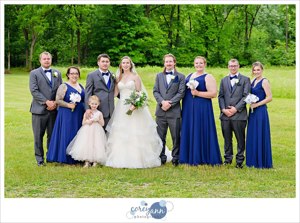 Bride and groom posing with their bridal party before the wedding at Amy's Rustic Event Center in Valley City Ohio taken outside in the grass on a sunny June day. The group is all smiling at the camera and the grouping is mixed and casual. 