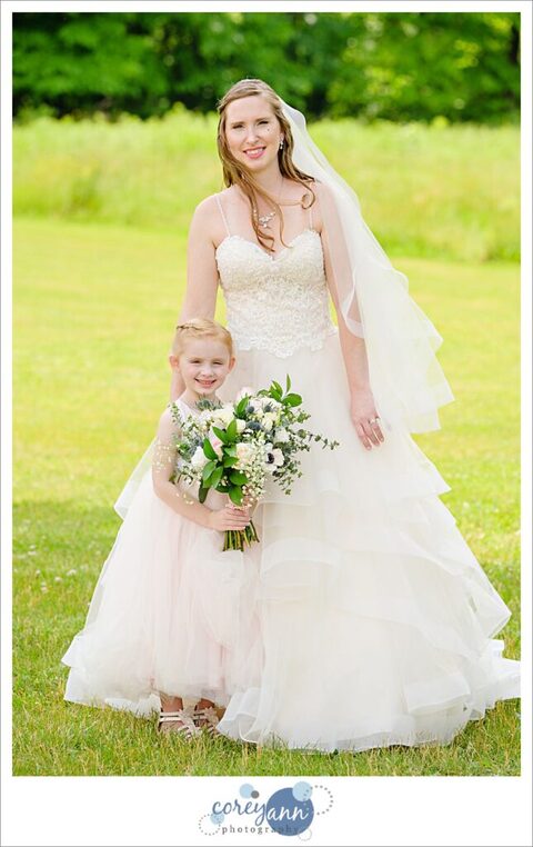 A bride and her daughter posing before the wedding ceremony at Amy's Rustic Event Center in Valley City, Ohio. The bride is wearing a beaded gown on top with frilly layers and the flower girl's dress echos the same style. 