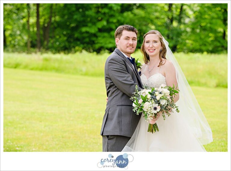 Bride and groom posing in the grass on a sunny day outside of Amy's Rustic Event Center in Valley City, Ohio