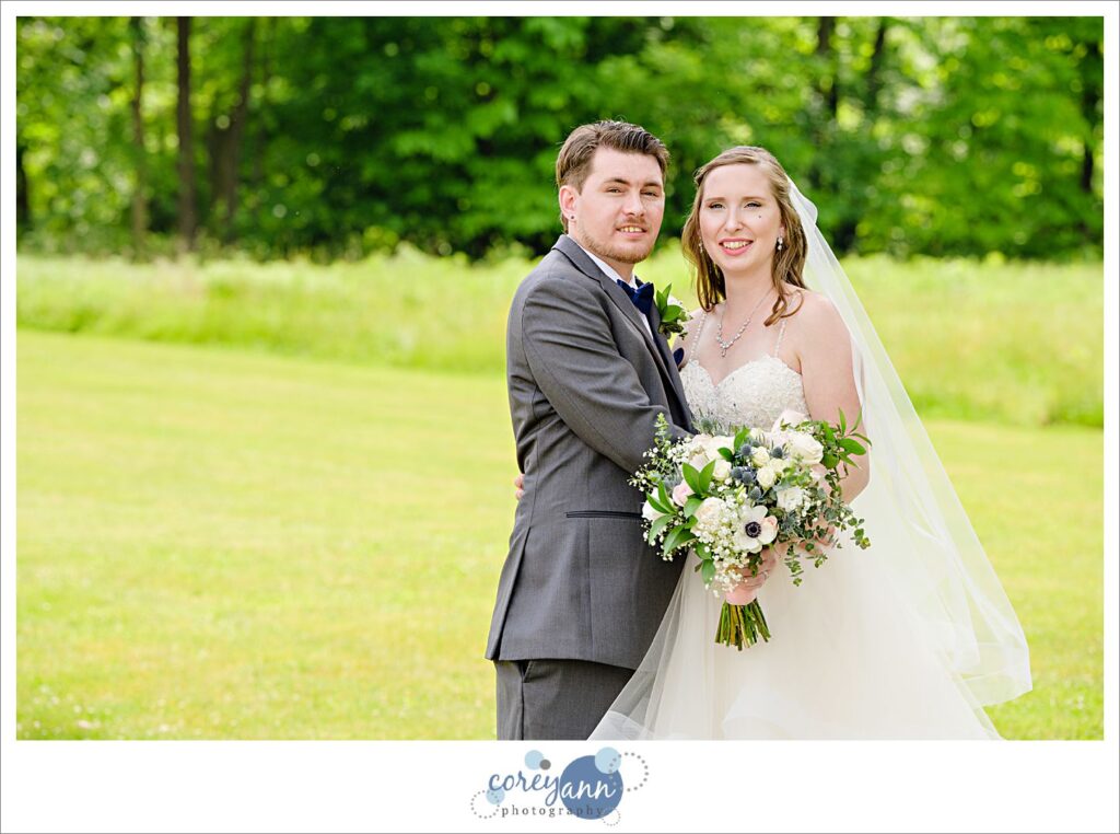 Bride and groom posing in the grass on a sunny day outside of Amy's Rustic Event Center in Valley City, Ohio