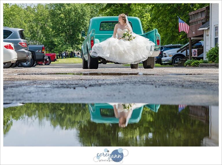 Bride riding to wedding ceremony in the bed of a teal antique truck at Amy's Rustic Event Center in Valley City, Ohio
