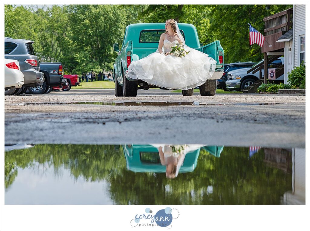 Bride riding to wedding ceremony in the bed of a teal antique truck at Amy's Rustic Event Center in Valley City, Ohio