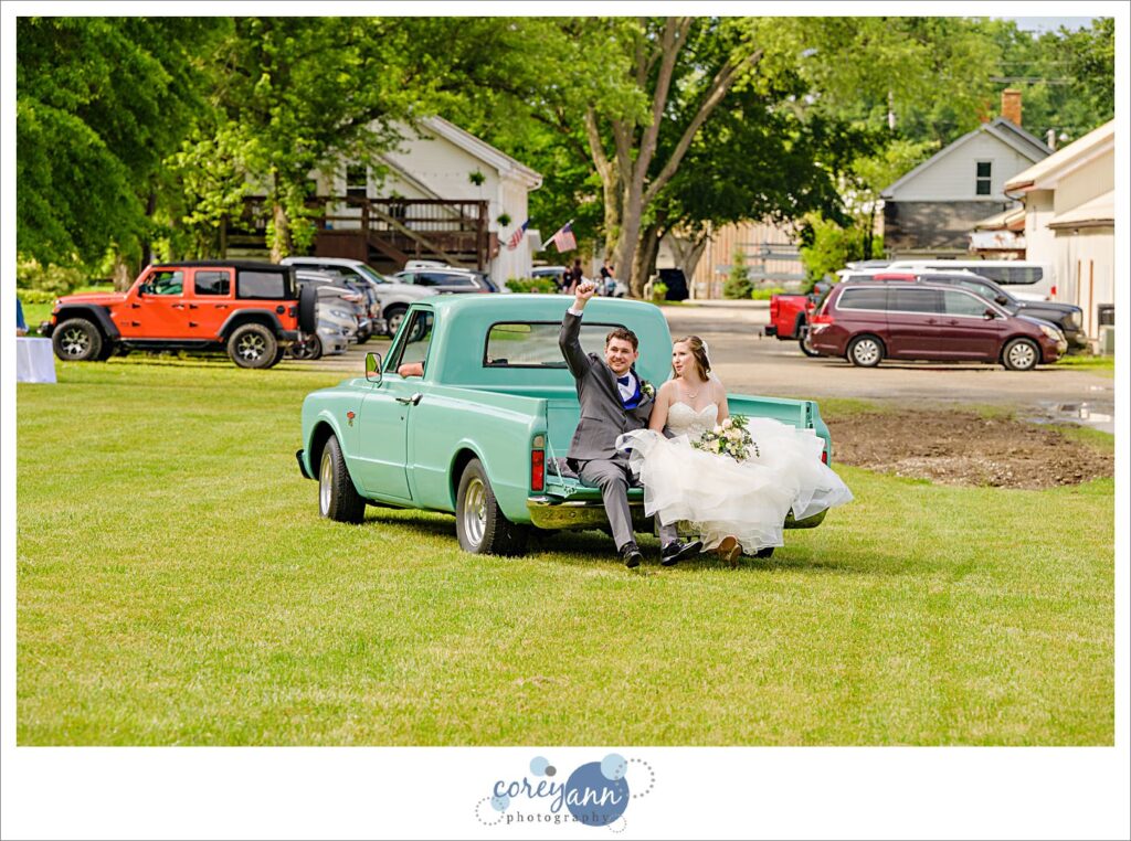 Bride and groom leaving outdoor wedding ceremony at Amy's Rustic Event Center in the bed of a rustic antique teal pickup truck.