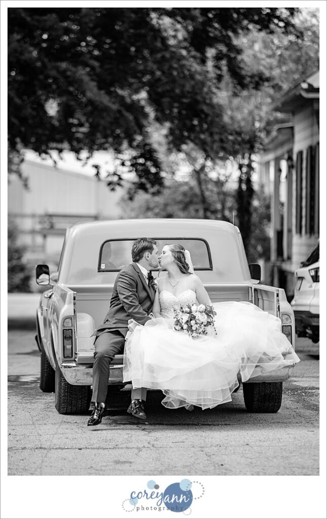Bride and groom leaving outdoor wedding ceremony at Amy's Rustic Event Center in the bed of a rustic antique teal pickup truck.