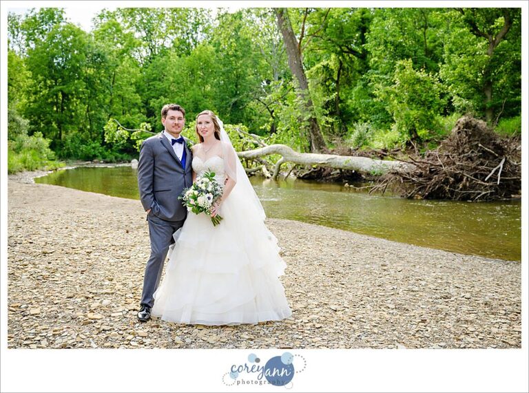 Bride and groom smiling at the camera and posing near Rocky River at Mill Stream Park in Valley City, Ohio after their wedding 